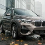 BMW X1 F48 garé en ville sous la pluie, vue trois quarts avant sur asphalte mouillé avec reflets urbains