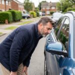 Homme d'âge moyen inspectant un SUV bleu en extérieur