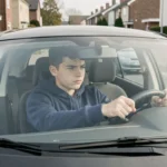 Jeune conducteur de 16 ans au volant d'une voiture sans permis dans une rue résidentielle, illustrant le permis AM