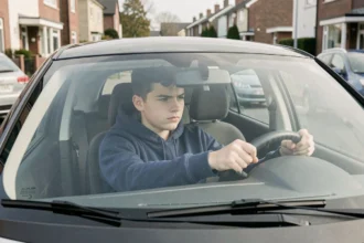 Jeune conducteur de 16 ans au volant d'une voiture sans permis dans une rue résidentielle, illustrant le permis AM