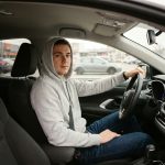 Jeune conducteur assis dans sa voiture tenant le volant, prêt à prendre la route pour la première fois en tant que conducteur assuré