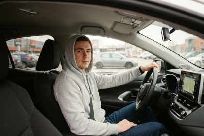 Jeune conducteur assis dans sa voiture tenant le volant, prêt à prendre la route pour la première fois en tant que conducteur assuré